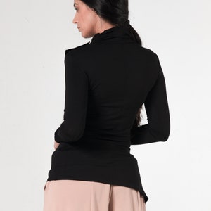 May include: A black long-sleeved shirt with a mock neck and a slightly longer back hem. The shirt is worn with a pair of light pink wide-leg pants.
