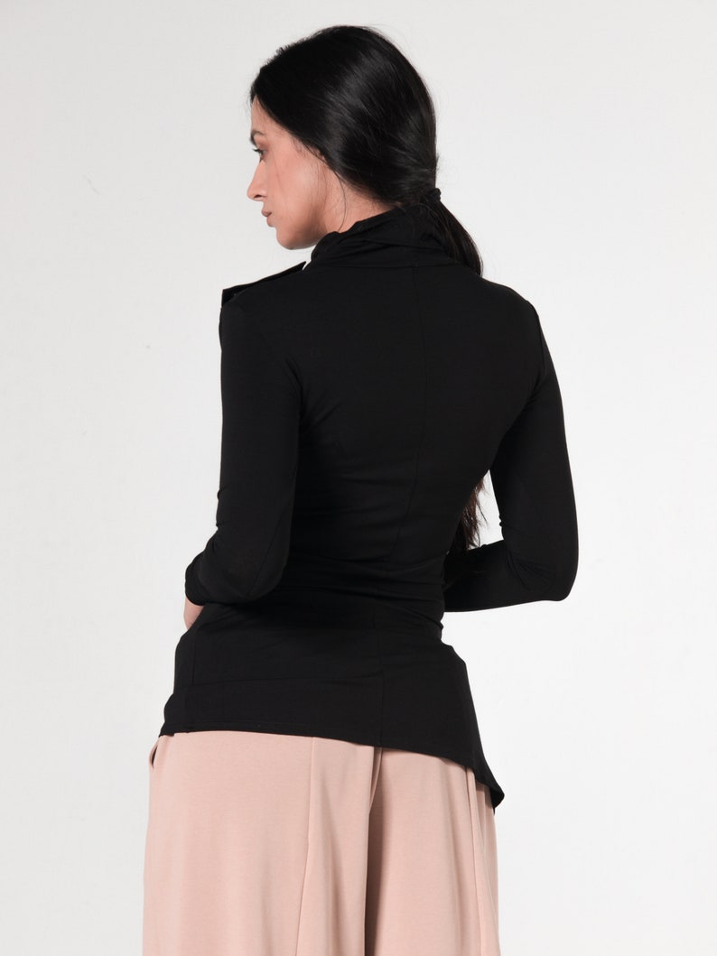 May include: A black long-sleeved shirt with a mock neck and a slightly longer back hem. The shirt is worn with a pair of light pink wide-leg pants.