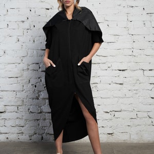 May include: A black long-sleeved dress with a high neckline and a zip closure. The dress has a high-low hemline and features a black fabric hood.