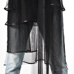 May include: Black sheer overlay with a layered design and a black trim. The overlay is worn over blue jeans.