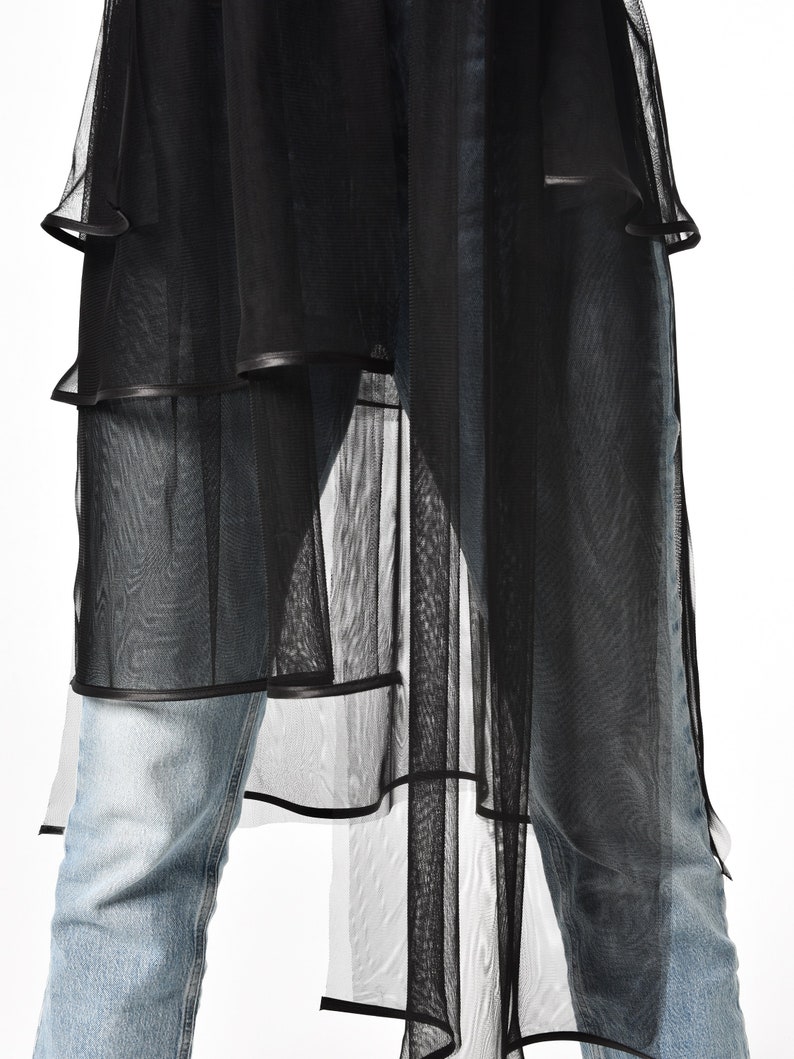 May include: Black sheer overlay with a layered design and a black trim. The overlay is worn over blue jeans.