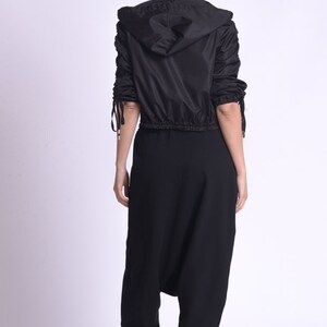 May include: A black hooded jacket with a drawstring waist and long sleeves. The jacket has a gathered detail on the sleeves. The model is wearing black pants and black sneakers.