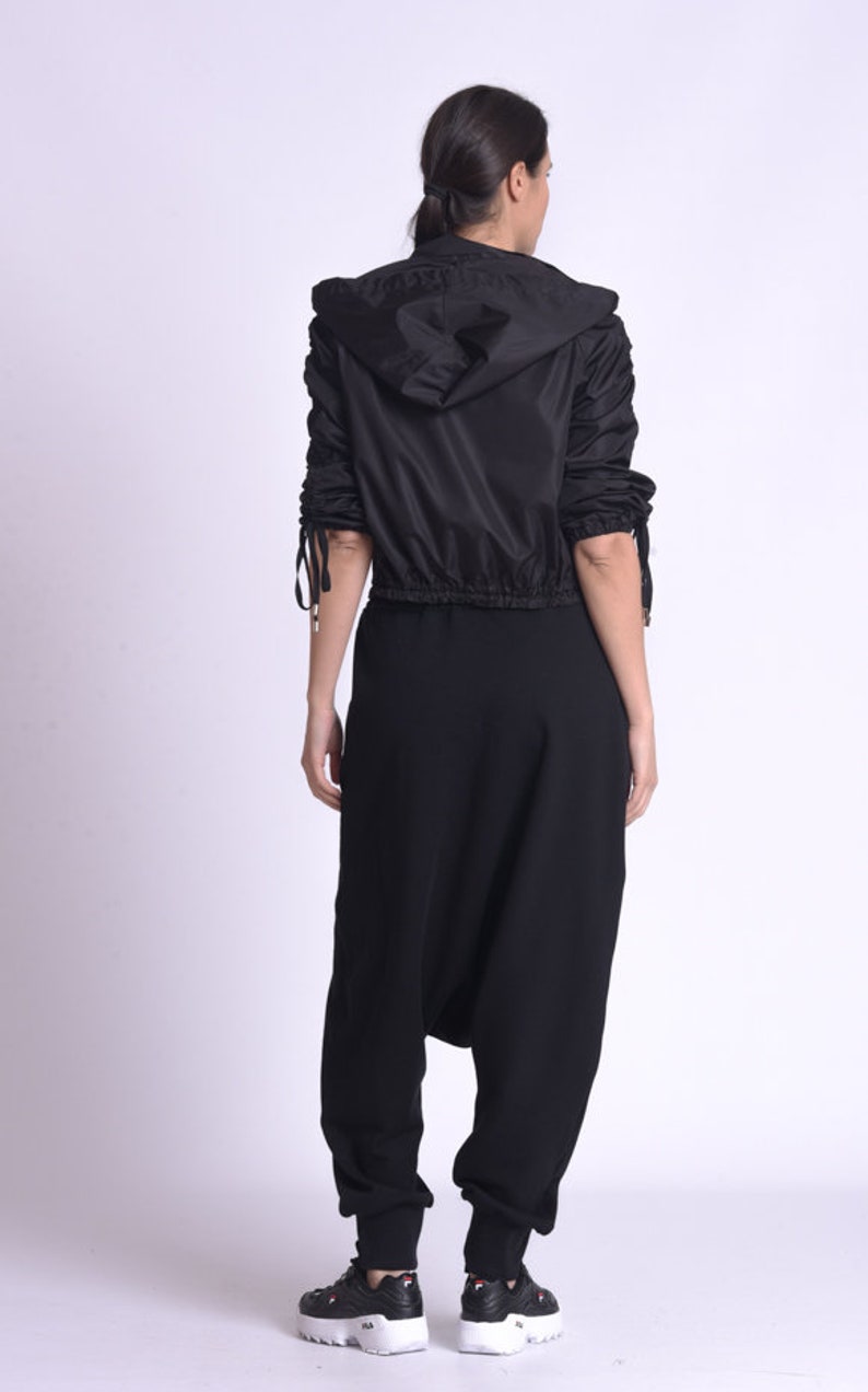 May include: A black hooded jacket with a drawstring waist and long sleeves. The jacket has a gathered detail on the sleeves. The model is wearing black pants and black sneakers.
