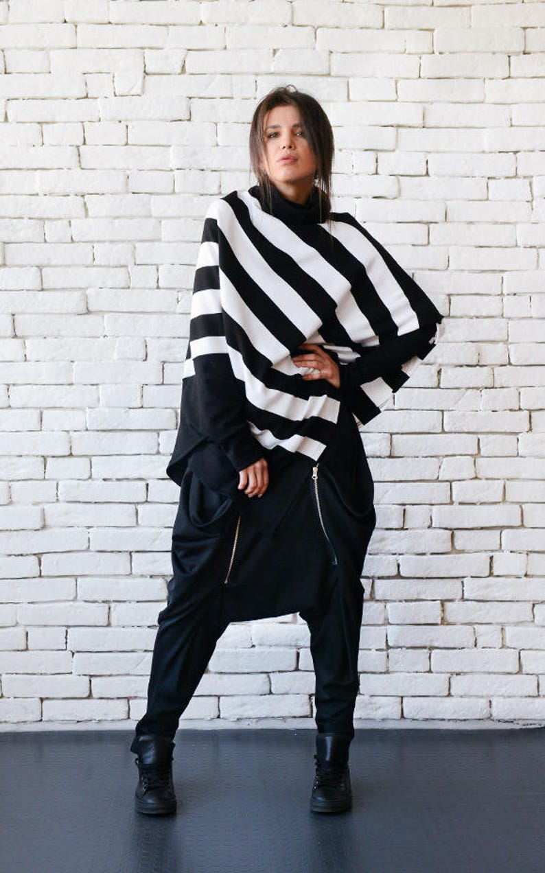 May include: A black and white striped sweater with a long sleeve and a loose fit. The sweater is worn over a black turtleneck shirt and black pants with a zipper detail.