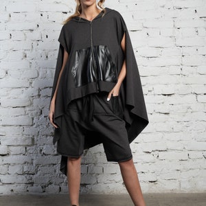 May include: A gray hooded sweatshirt with a black leather pocket and a long, flowing back. The sweatshirt is paired with matching gray shorts.