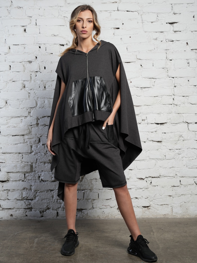 May include: A gray hooded sweatshirt with a black leather pocket and a long, flowing back. The sweatshirt is paired with matching gray shorts.