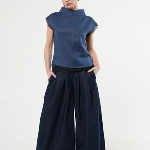 May include: A woman wearing a blue linen top with a high neckline and a pair of dark blue wide-leg denim trousers.