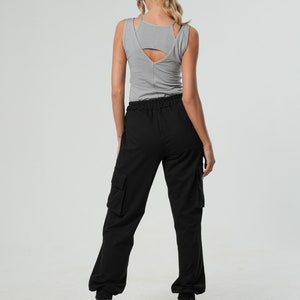 May include: A woman wearing a gray tank top and black cargo pants with a drawstring waist. She is wearing black heels.