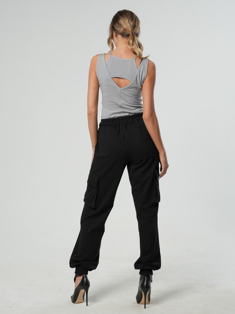 May include: A woman wearing a gray tank top and black cargo pants with a drawstring waist. She is wearing black heels.