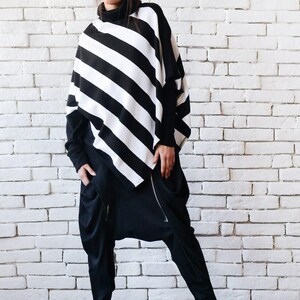 May include: A black and white striped tunic top with a long sleeve and a high neck. The top is paired with black pants with a zipper detail and black shoes.