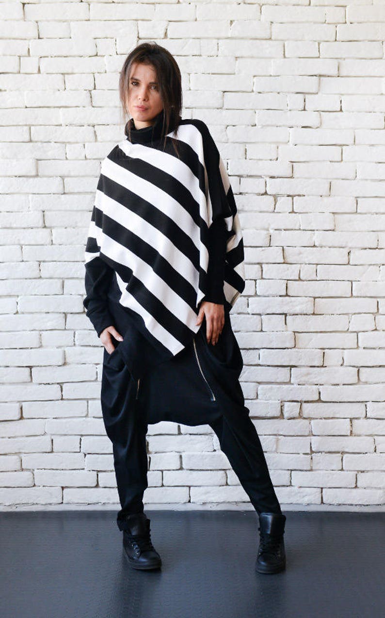 May include: A black and white striped tunic top with a long sleeve and a high neck. The top is paired with black pants with a zipper detail and black shoes.