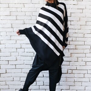May include: A black and white striped tunic with a long, flowing silhouette. The tunic has a high neck and a relaxed fit. The model is wearing black pants and black high-top sneakers.