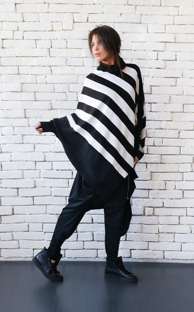 May include: A black and white striped tunic with a long, flowing silhouette. The tunic has a high neck and a relaxed fit. The model is wearing black pants and black high-top sneakers.
