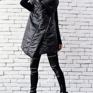May include: A black quilted vest with a zipper closure and a high collar. The vest is worn over a black long-sleeved shirt and black leggings. The person is wearing black platform boots and sunglasses.
