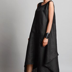 May include: A black linen dress with a loose, asymmetrical fit and a single pocket on the left side. The dress is sleeveless and has a round neckline.