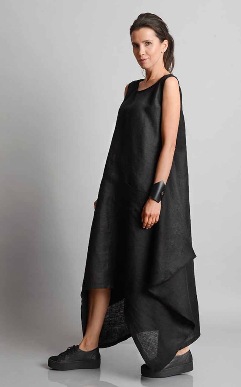 May include: A black linen dress with a loose, asymmetrical fit and a single pocket on the left side. The dress is sleeveless and has a round neckline.