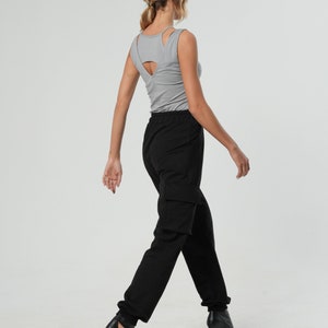 May include: A woman wearing a gray tank top with a cut-out back and black cargo pants. She is wearing black heeled sandals.