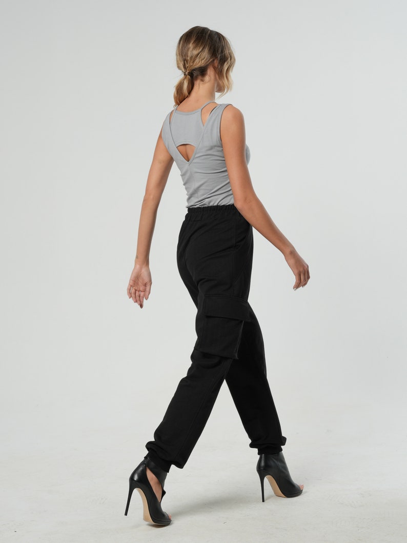 May include: A woman wearing a gray tank top with a cut-out back and black cargo pants. She is wearing black heeled sandals.