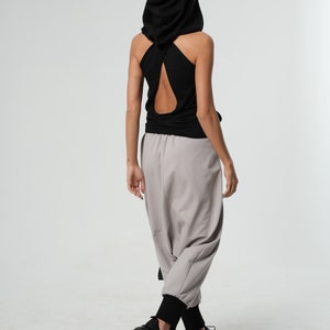 May include: A black hooded tank top with a cut-out back design. The top is paired with light gray pants and black sneakers.