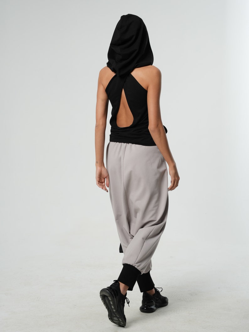 May include: A black hooded tank top with a cut-out back design. The top is paired with light gray pants and black sneakers.