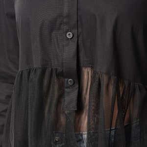 May include: Black long-sleeved shirt with a sheer mesh overlay. The shirt has a button-up front and a ruffled hem.