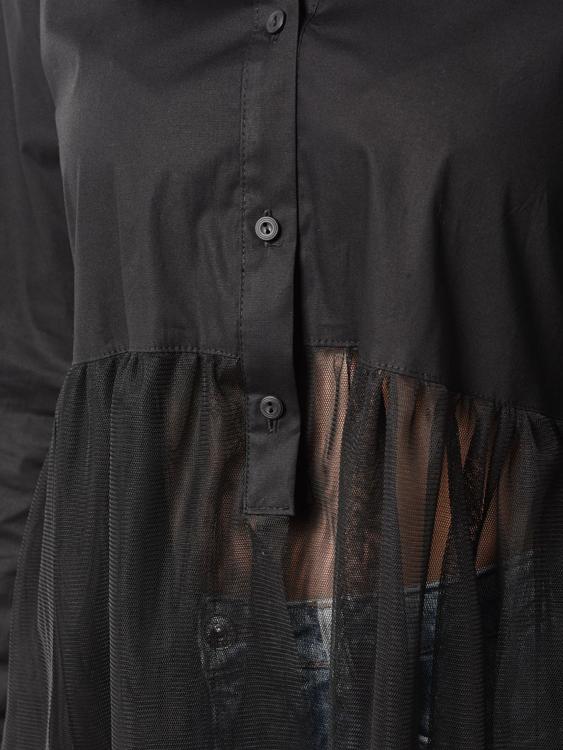 May include: Black long-sleeved shirt with a sheer mesh overlay. The shirt has a button-up front and a ruffled hem.