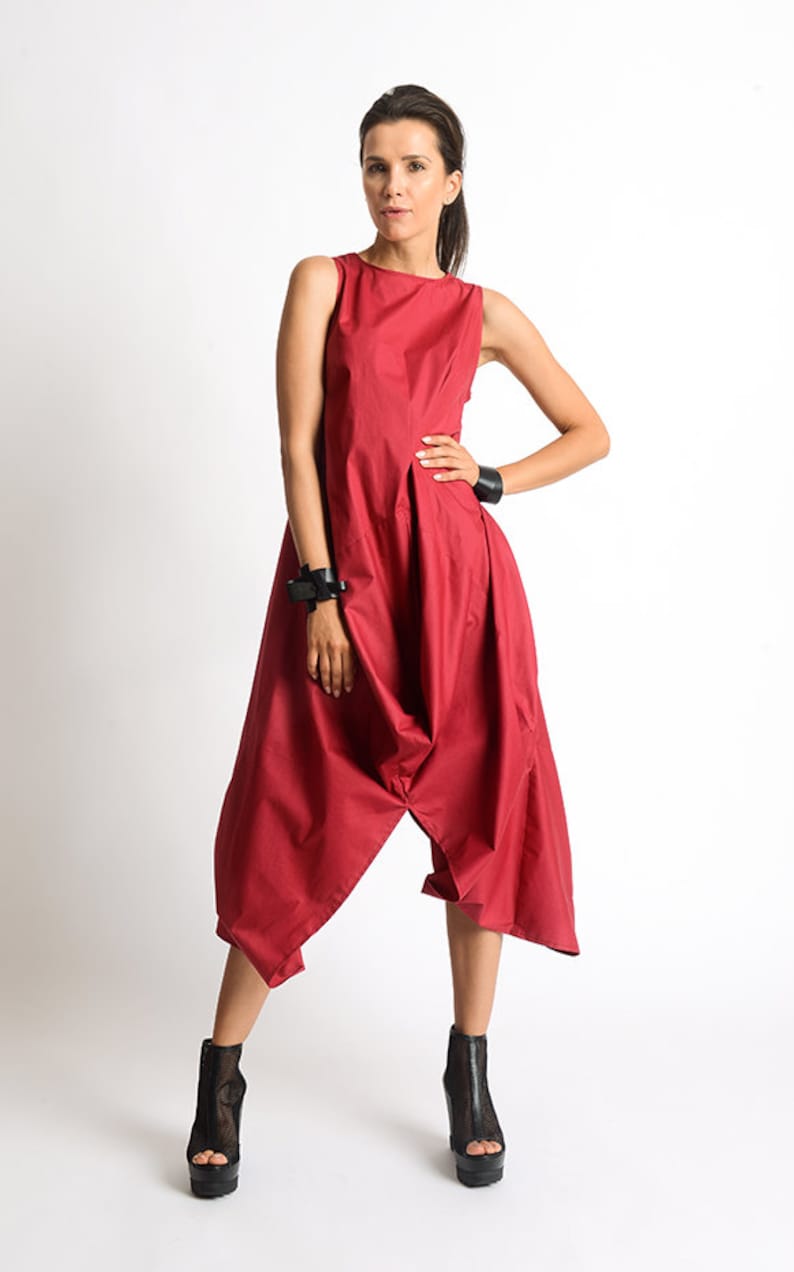Peut inclure: Une combinaison rouge sans manches &agrave; la coupe ample et fluide. La combinaison a une jambe large et une taille fronc&eacute;e. Le mannequin porte des talons compens&eacute;s noirs.