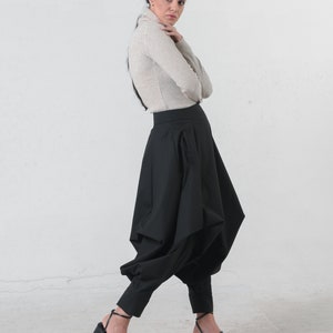 May include: A woman wearing a beige turtleneck sweater and black pants with a unique, gathered design. She is wearing black heeled sandals.