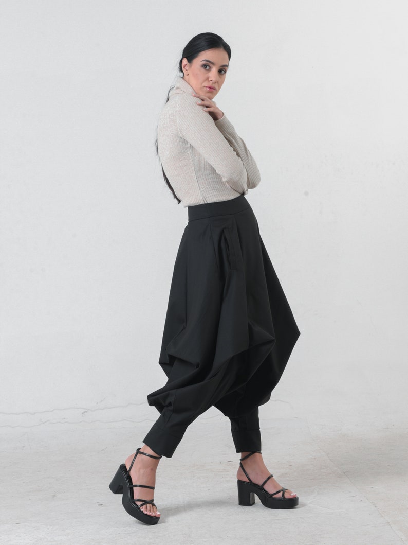 May include: A woman wearing a beige turtleneck sweater and black pants with a unique, gathered design. She is wearing black heeled sandals.