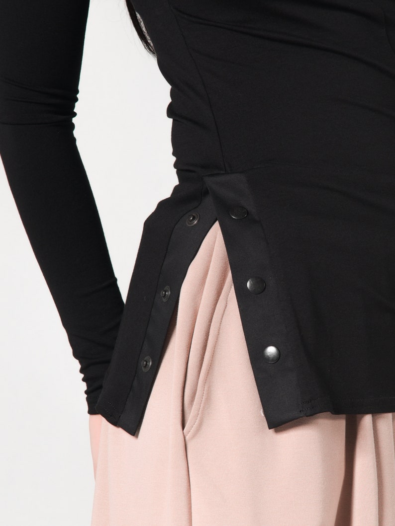 May include: Black long-sleeved shirt with a side panel of black fabric and snap buttons. The shirt is worn with a light pink skirt.