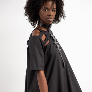 May include: A black dress with a cut-out design at the shoulders and a leather strap with metal buckles across the chest.