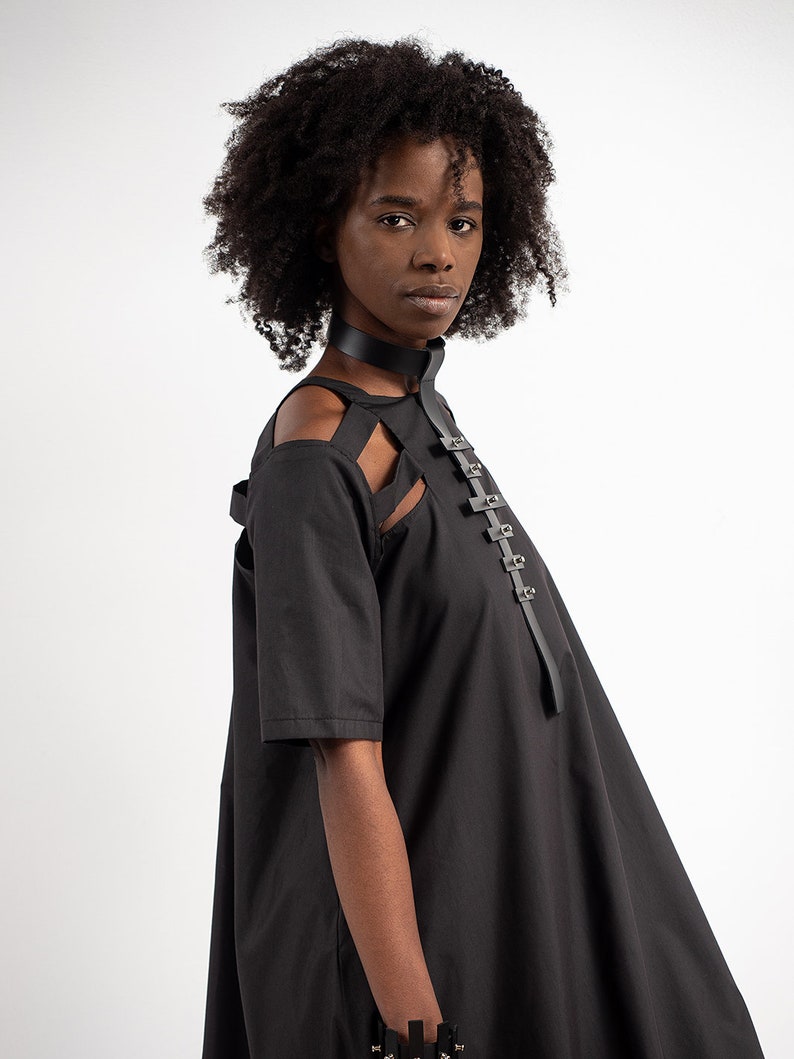 May include: A black dress with a cut-out design at the shoulders and a leather strap with metal buckles across the chest.