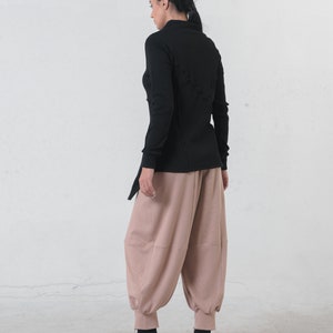 May include: A black long-sleeved shirt with a criss-cross design on the back. The shirt is paired with loose-fitting, light brown pants.