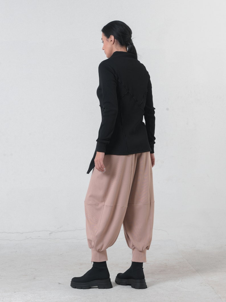 May include: A black long-sleeved shirt with a criss-cross design on the back. The shirt is paired with loose-fitting, light brown pants.