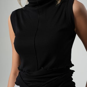 Op de afbeelding: Een zwart mouwloos shirt met een hoge hals en een gerimpelde zoom.