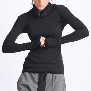May include: A black long-sleeved shirt with a mock neck and thumbholes. The shirt is paired with gray pants with a black belt.