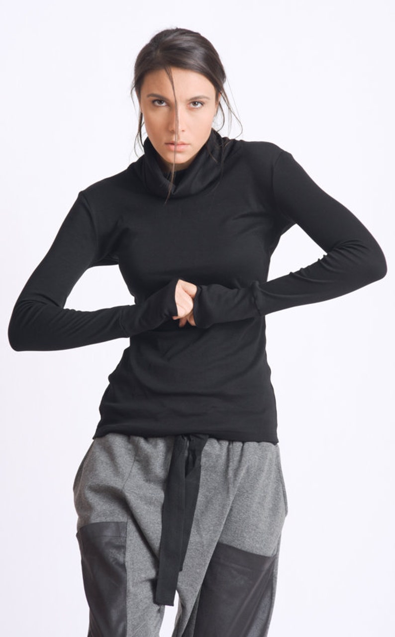 May include: A black long-sleeved shirt with a mock neck and thumbholes. The shirt is paired with gray pants with a black belt.