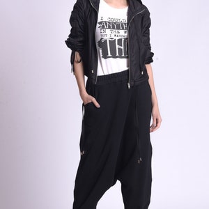 May include: A woman wearing a black jacket with a white t-shirt that says "I could have anything in the world but I wanted this". She is wearing black pants with a drawstring waist and black sneakers.