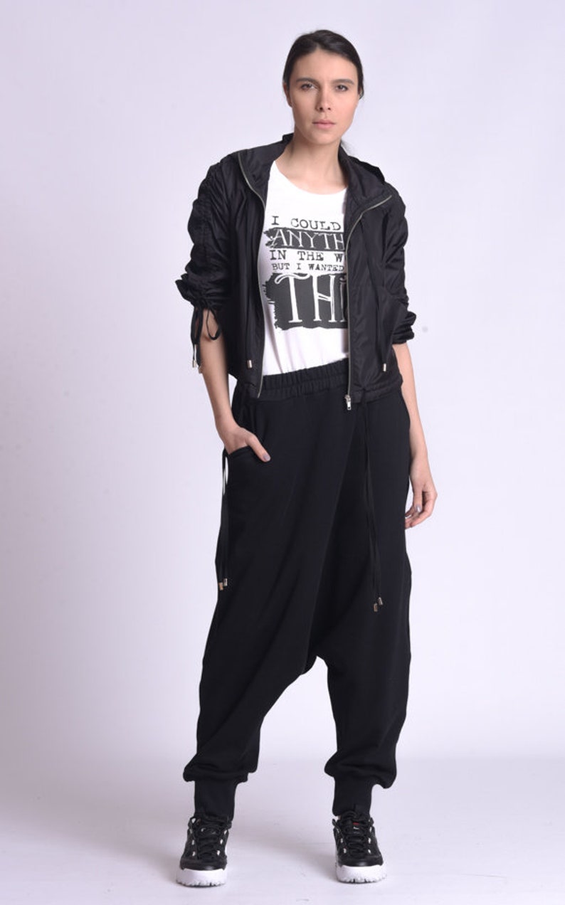May include: A woman wearing a black jacket with a white t-shirt that says "I could have anything in the world but I wanted this". She is wearing black pants with a drawstring waist and black sneakers.