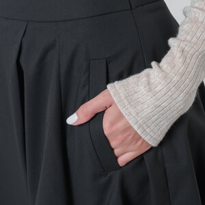 May include: Black skirt with a pleated front and a side pocket. The skirt is made of a smooth, wrinkle-resistant fabric.