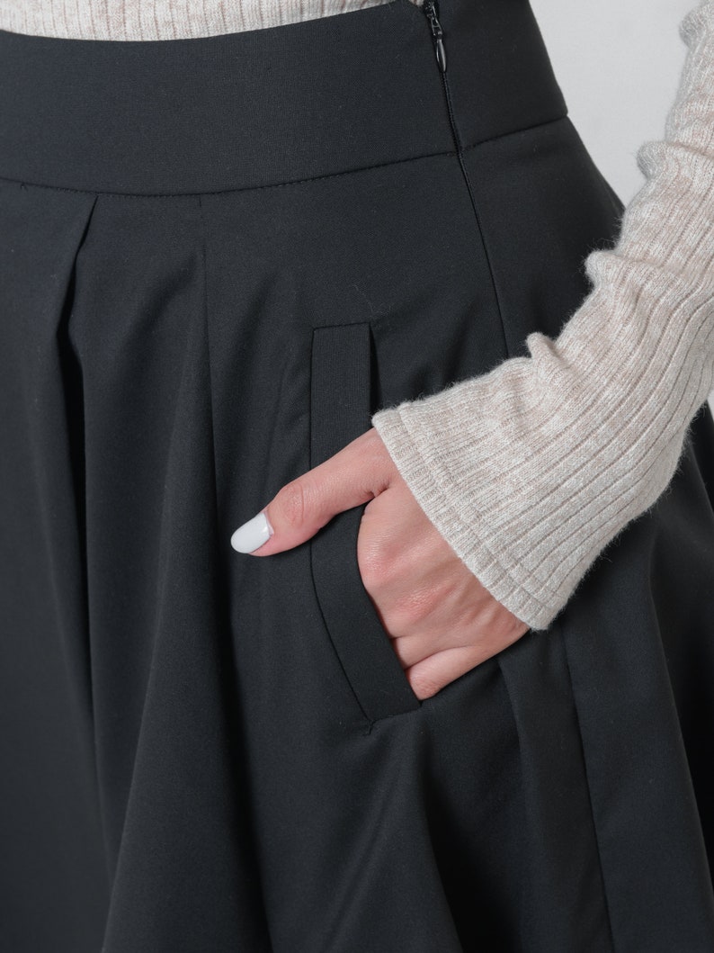 May include: Black skirt with a pleated front and a side pocket. The skirt is made of a smooth, wrinkle-resistant fabric.