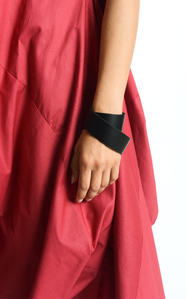 May include: A black leather bracelet with a simple, modern design. The bracelet is wrapped around the wrist twice and has a clean, minimalist aesthetic.