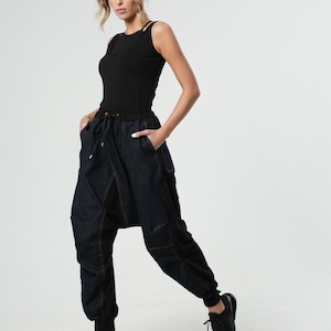 May include: A woman wearing a black tank top and dark blue denim pants with a unique design. The pants have a loose fit and a drawstring waist.