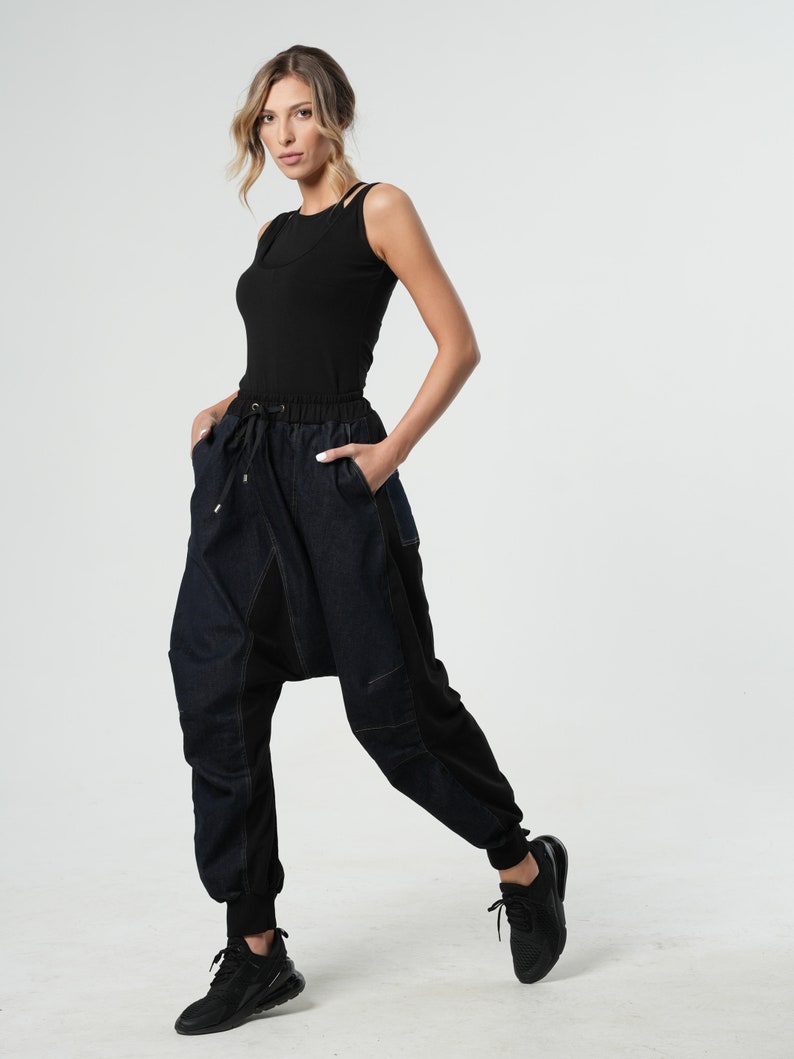 May include: A woman wearing a black tank top and dark blue denim pants with a unique design. The pants have a loose fit and a drawstring waist.