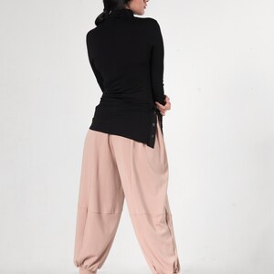 May include: A black turtleneck top with a side slit and a pair of light pink, wide-leg pants.