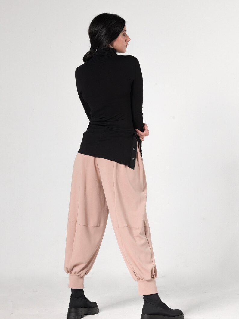 May include: A black turtleneck top with a side slit and a pair of light pink, wide-leg pants.