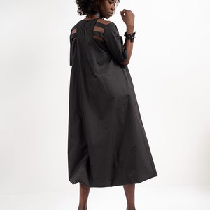 May include: A black midi dress with a cut-out back detail. The dress has a loose fit and falls to the mid-calf. The model is wearing black platform sandals.