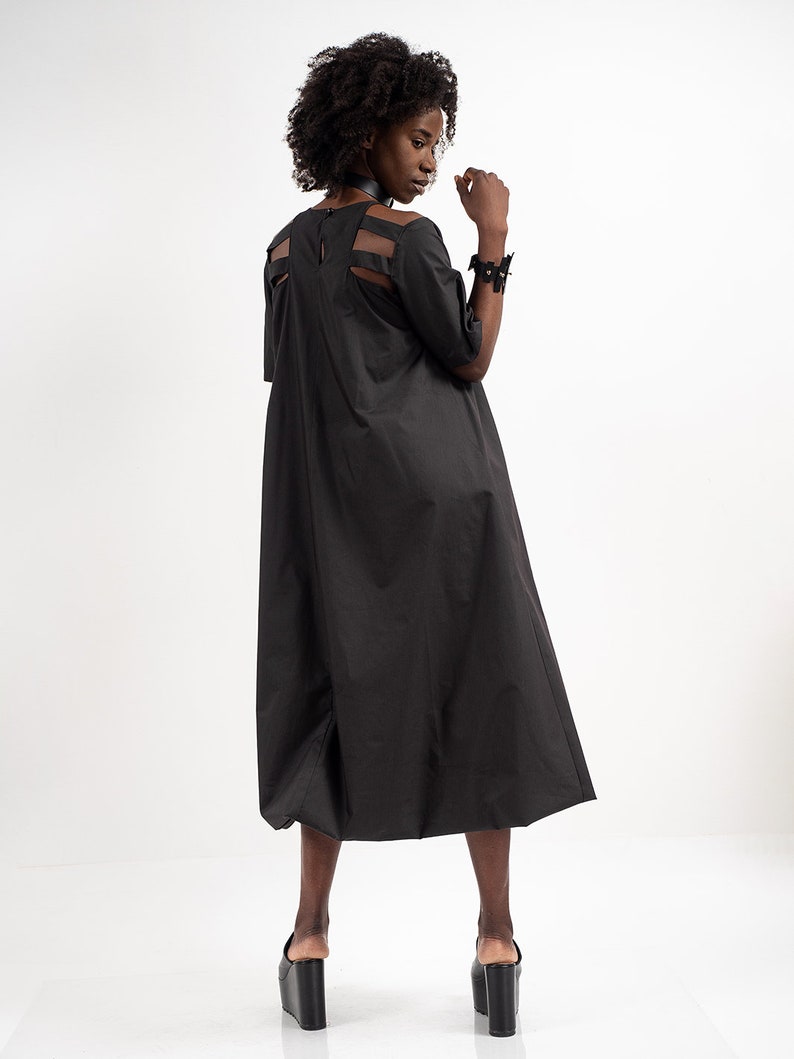 May include: A black midi dress with a cut-out back detail. The dress has a loose fit and falls to the mid-calf. The model is wearing black platform sandals.