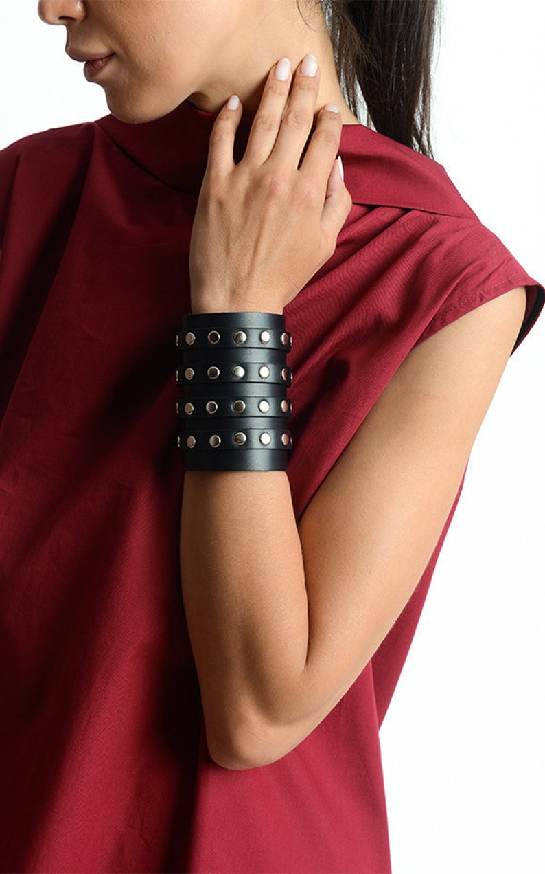 May include: A black leather bracelet with silver studs. The bracelet is wide and has multiple layers.