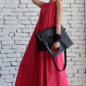 May include: A woman wearing a bright pink sleeveless maxi dress and black sunglasses holds a black leather tote bag with a long strap.